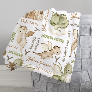 May include: White baby blanket with a repeating pattern of green and brown dragons, clouds, and the names "Yohan Pierre" and "Yohan".