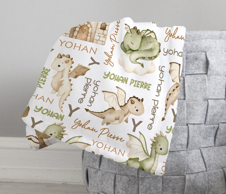 May include: White baby blanket with a repeating pattern of green and brown dragons, clouds, and the names "Yohan Pierre" and "Yohan".