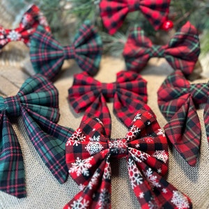 May include: A collection of eight red and green plaid bows with snowflake patterns. The bows are made of fabric and are tied with a ribbon.