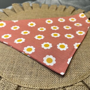 May include: A pink bandana with a white daisy pattern. The bandana is on a brown burlap surface.