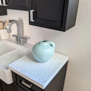Può includere: Una tazza di ceramica bianca con manico nero e la scritta "But First, Coffee" in grassetto nero. La tazza è posta su uno sfondo sfocato, che suggerisce un'atmosfera accogliente.
