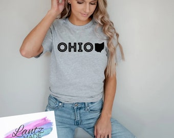 Könnte beinhalten: Ein graues T-Shirt mit dem Wort "OHIO" in Schwarz bedruckt, rechts daneben eine schwarze Umrandung des Bundesstaates Ohio.