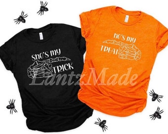May include: Two black and orange t-shirts with a skeleton hand graphic and the text "She's my trick" and "He's my treat".
