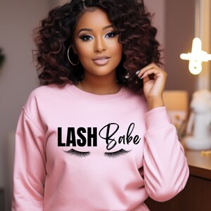 May include: A pink sweatshirt with the text "LASH Babe" in black lettering and a pair of eyelashes on either side of the text.