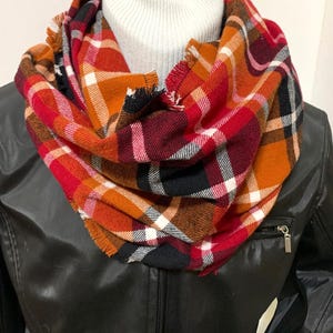 May include: A red, orange, black, and white plaid infinity scarf with frayed edges.