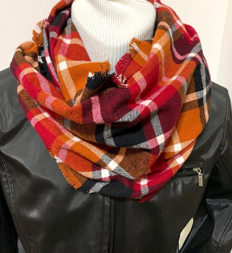 May include: A red, orange, black, and white plaid infinity scarf with frayed edges.