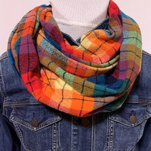 May include: A colorful plaid infinity scarf with a mix of red, orange, yellow, green, blue, and brown hues. The scarf is made of a soft, warm fabric and is perfect for keeping you cozy in the colder months.