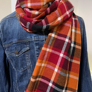 May include: A red, orange, black, and white plaid scarf. The scarf is folded and draped over a denim jacket.