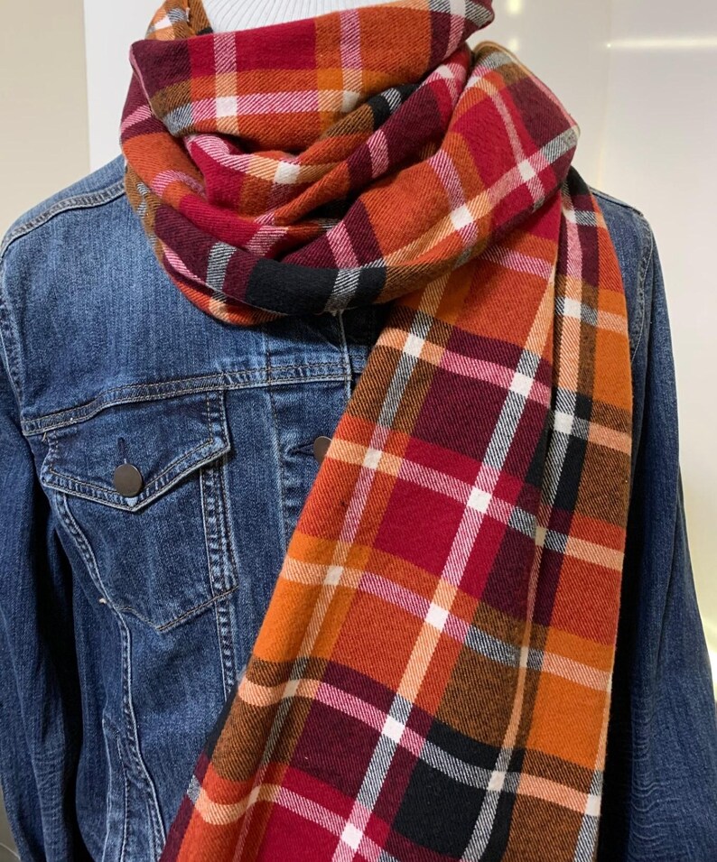 May include: A red, orange, black, and white plaid scarf. The scarf is folded and draped over a denim jacket.