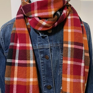 May include: A red, orange, white, and black plaid scarf. The scarf is folded and draped around a denim jacket.