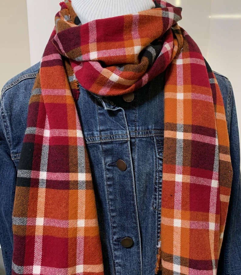 May include: A red, orange, white, and black plaid scarf. The scarf is folded and draped around a denim jacket.