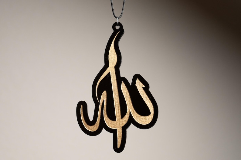 May include: A black and gold car air freshener with the word "Allah" written in Arabic calligraphy.