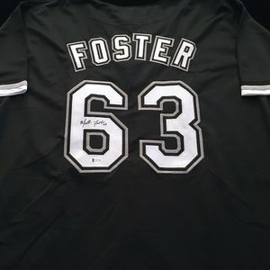 May include: Black baseball jersey with white lettering. The name "FOSTER" and the number "63" are on the back of the jersey. The jersey is signed in black ink.