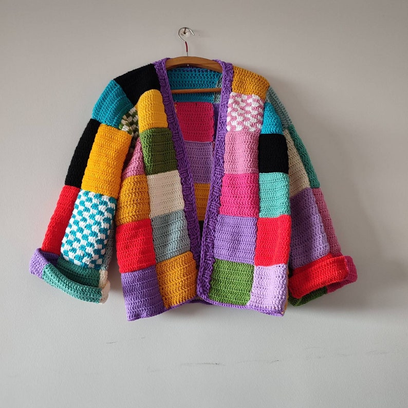 Puede incluir: Una chaqueta de punto de ganchillo colorida con un dise&ntilde;o de patchwork en tonos de morado, rosa, rojo, verde, azul y amarillo.