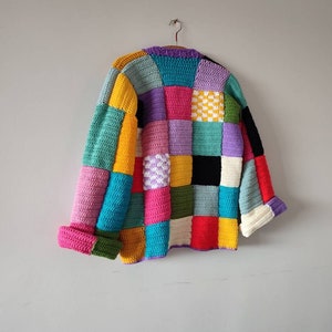 Puede incluir: Una chaqueta de punto de ganchillo colorida con un dise&ntilde;o de patchwork. La chaqueta est&aacute; hecha de cuadrados de varios colores, incluyendo rosa, azul, verde, amarillo y morado.