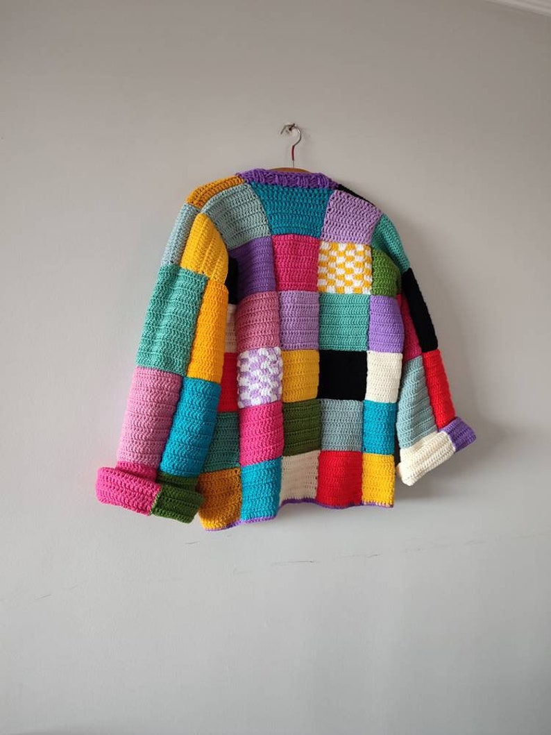 Puede incluir: Una chaqueta de punto de ganchillo colorida con un dise&ntilde;o de patchwork. La chaqueta est&aacute; hecha de cuadrados de varios colores, incluyendo rosa, azul, verde, amarillo y morado.