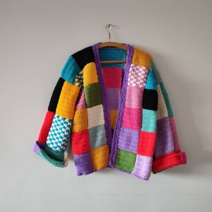 Puede incluir: Un c&aacute;rdigan de crochet colorido con un dise&ntilde;o de patchwork en tonos de rosa, azul, verde, amarillo y morado. El c&aacute;rdigan tiene un cierre de botones en la parte delantera y mangas largas.
