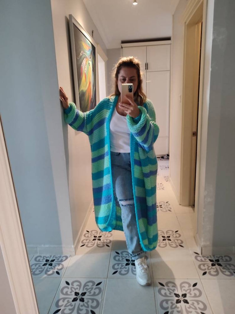 May include: Long turquoise and light green striped cardigan. The cardigan is knitted and has a relaxed fit. It is open-front and has long sleeves. The cardigan is shown on a mannequin in a hallway setting.She is 1.60cm.