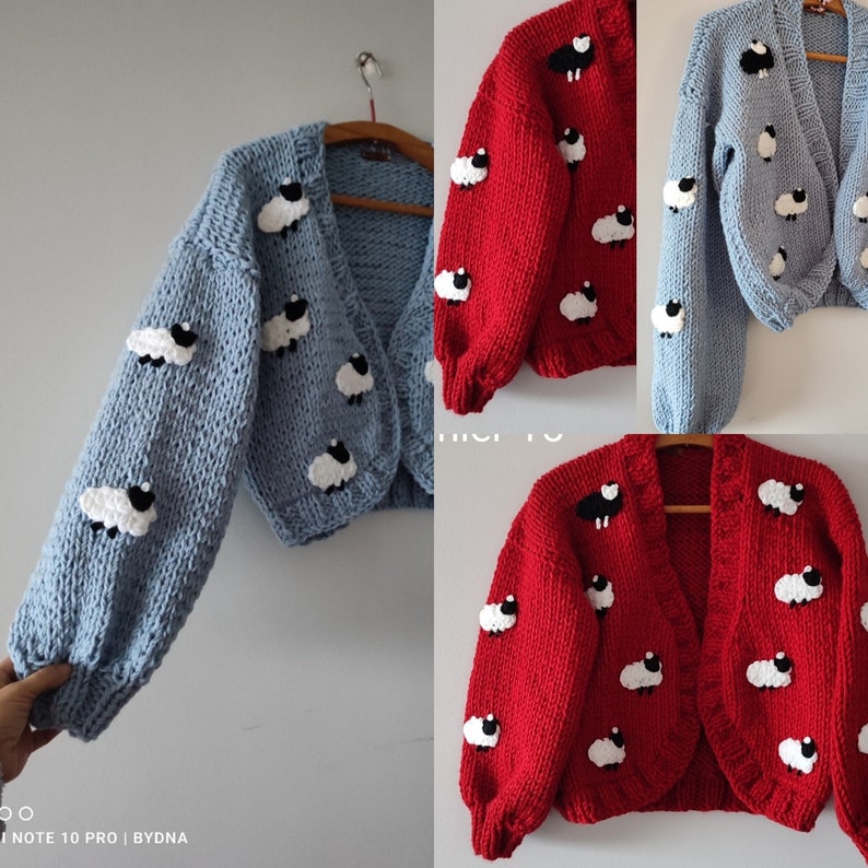 K&ouml;nnte beinhalten: Hellblau und rote Strickjacke mit wei&szlig;en und schwarzen Schafapplikationen. Die Strickjacke hat lange &Auml;rmel und einen verk&uuml;rzten Schnitt. Die Schafe sind gleichm&auml;&szlig;ig &uuml;ber dem Kleidungsst&uuml;ck verteilt.