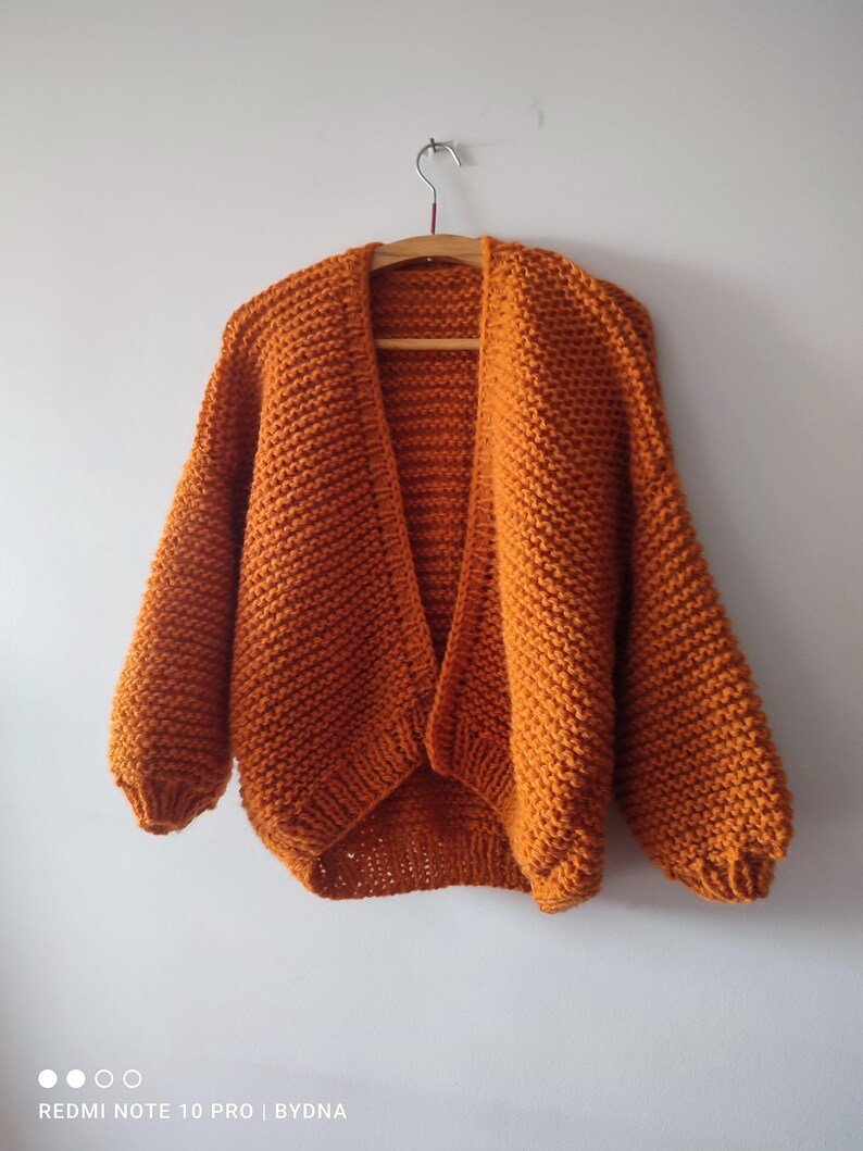 Puede incluir: Un c&aacute;rdigan de punto grueso en un vibrante color naranja quemado. Esta prenda abierta en la parte delantera presenta mangas largas y voluminosas con pu&ntilde;os acanalados y un patr&oacute;n de punto bobo texturizado en toda su superficie.