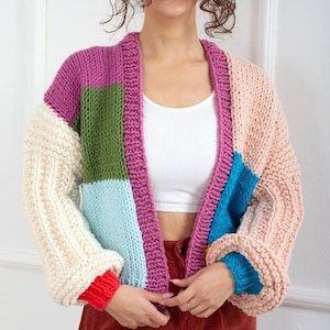 May include: A colorful knitted cardigan with a patchwork design. The cardigan has a pink, green, blue, and white color scheme. The cardigan is open in the front and has long sleeves.