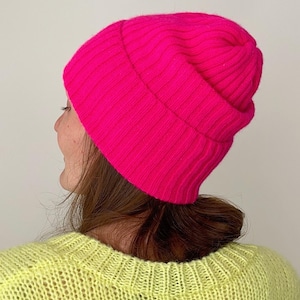 Könnte beinhalten: Eine leuchtend pinkfarbene Mütze aus weichem, geripptem Strick. Die Mütze ist oben umgeklappt und erzeugt so einen lässigen Look.