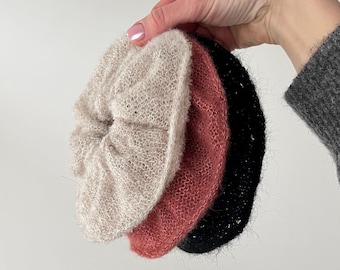 May include: Three hair scrunchies in different colors: beige, pink, and black. The scrunchies are made of a soft, fuzzy material.