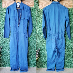 May include: A blue denim jumpsuit with a zipper closure and a single chest pocket. The jumpsuit has long sleeves and a relaxed fit.