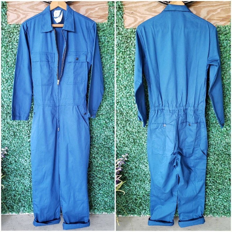 May include: A blue denim jumpsuit with a zipper closure and a single chest pocket. The jumpsuit has long sleeves and a relaxed fit.