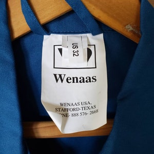 May include: A white tag with the text "Wenaas" and "Wenaas USA, Stafford-Texas, Phone-888 576-2668" on a blue work shirt. The tag also has a size label that says "US 32".