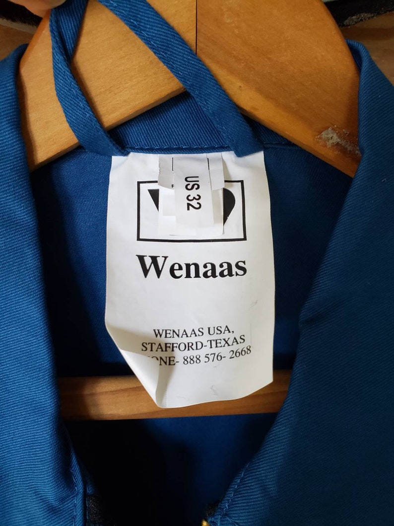 May include: A white tag with the text "Wenaas" and "Wenaas USA, Stafford-Texas, Phone-888 576-2668" on a blue work shirt. The tag also has a size label that says "US 32".