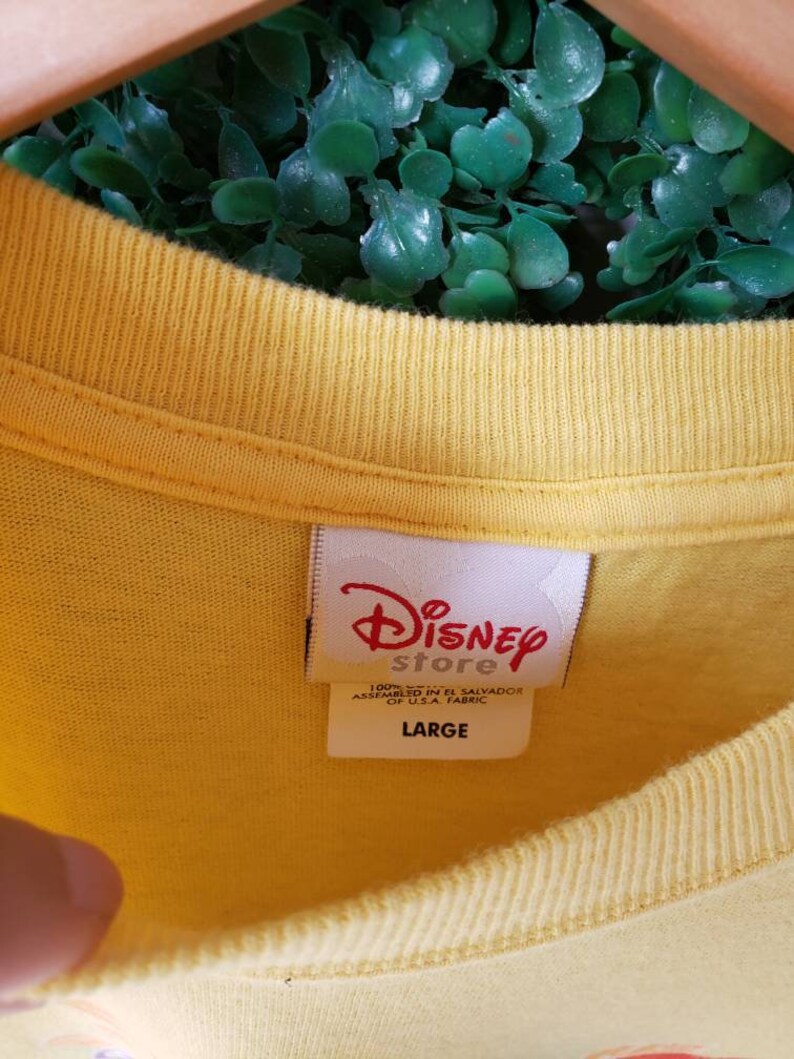 May include: Yellow t-shirt with a white tag that says "Disney Store" and "100% Cotton Assembled in El Salvador of U.S.A. Fabric" and "Large".