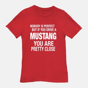 May include: Red t-shirt with white text that reads "Nobody is perfect but if you drive a Mustang you are pretty close."