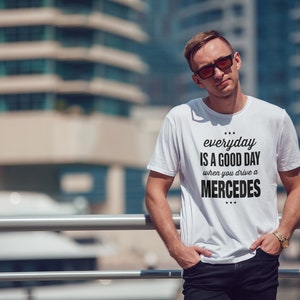 Op de afbeelding: Een wit T-shirt met zwarte tekst die "everyday is a good day when you drive a MERCEDES" zegt.
