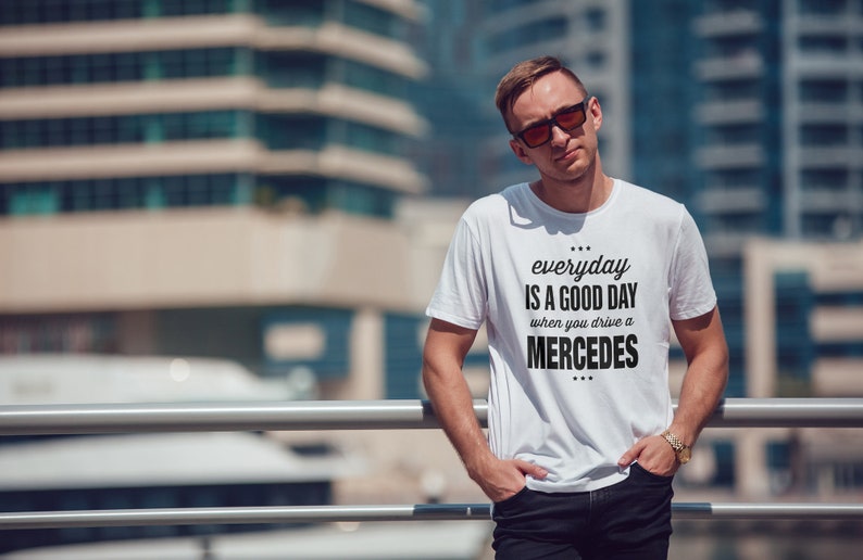 Op de afbeelding: Een wit T-shirt met zwarte tekst die "everyday is a good day when you drive a MERCEDES" zegt.