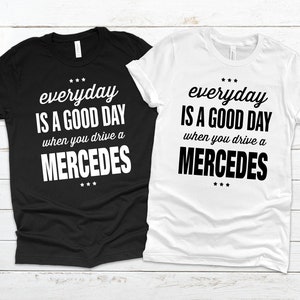 Op de afbeelding: Twee T-shirts met de tekst "*** everyday IS A GOOD DAY when you drive a MERCEDES ***" erop gedrukt. Een T-shirt is zwart en de andere is wit.