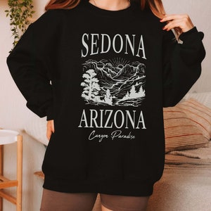 May include: Black sweatshirt with a white graphic design of a mountain landscape and the text "Sedona Arizona Canyon Paradise".