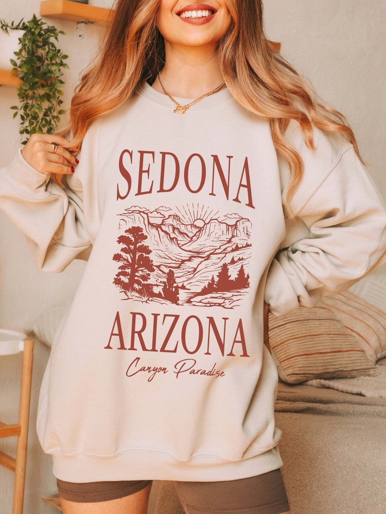 May include: A beige sweatshirt with a red graphic print of a mountain landscape and the text "Sedona Arizona Canyon Paradise".