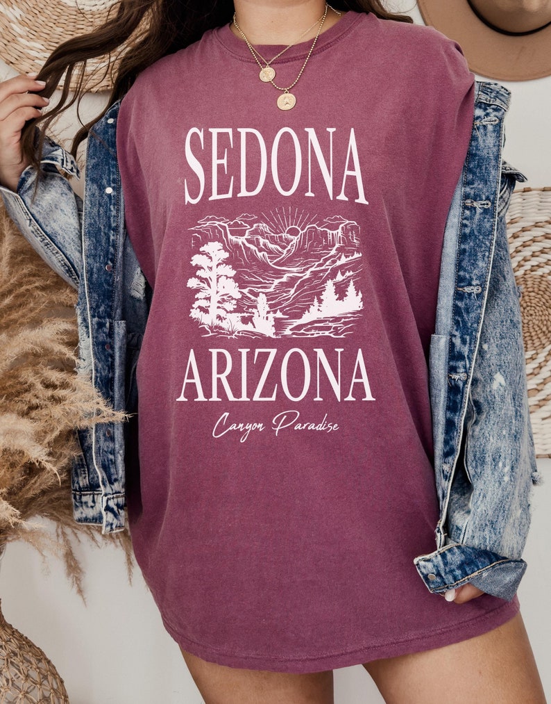 May include: A maroon oversized t-shirt with a white graphic design featuring the text "Sedona Arizona Canyon Paradise" and a stylized image of a mountain landscape.
