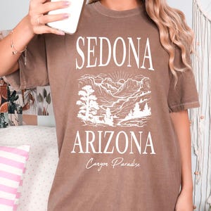 May include: A brown oversized t-shirt with a white graphic print of a mountain landscape and the text "Sedona Arizona Canyon Paradise".
