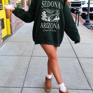 May include: A dark green sweatshirt with a white graphic print of a mountain landscape and the text "Sedona Arizona Canyon Paradise".
