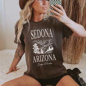 May include: A dark gray t-shirt with a white graphic of a mountain landscape and the text "Sedona Arizona Canyon Paradise".