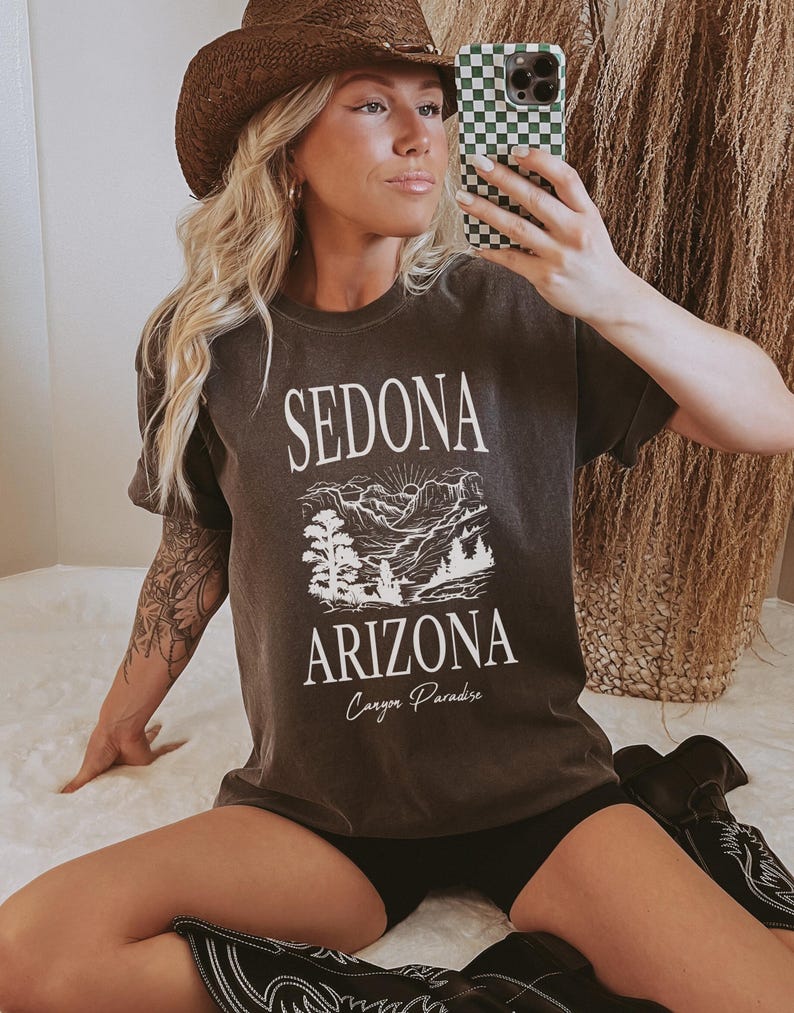 May include: A dark gray t-shirt with a white graphic of a mountain landscape and the text "Sedona Arizona Canyon Paradise".