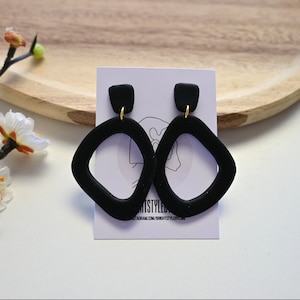 May include: A pair of black geometric dangle earrings with gold hooks. The earrings are shaped like a rounded rectangle with a cutout in the centre.