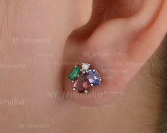 May include: Close-up of a person's ear wearing a small cluster of gemstone earrings. The earrings feature a mix of green, purple, blue, and white gemstones set in a silver metal.