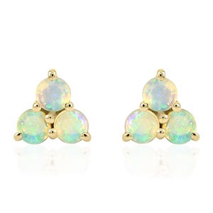 Puede incluir: Un par de pendientes de oro, cada uno con tres piedras de ópalo redondas e iridiscentes dispuestas en un racimo triangular. Los ópalos muestran colores blancos, amarillos y toques de azul y verde. Los pendientes están sobre un fondo blanco.