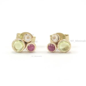 May include: A pair of gold stud earrings with three small gemstones each. The earrings feature a light green, a pink, and a white gemstone.