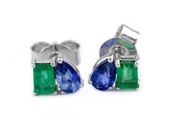 May include: A pair of silver stud earrings with a blue pear-shaped sapphire and a green emerald gemstone.