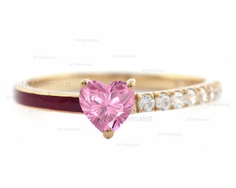May include: A gold ring with a pink heart-shaped gemstone and a band of small white gemstones. The band is also accented with a thin red line.