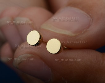 May include: A pair of gold-toned minimalist stud earrings. The earrings are round and have a smooth, polished finish.